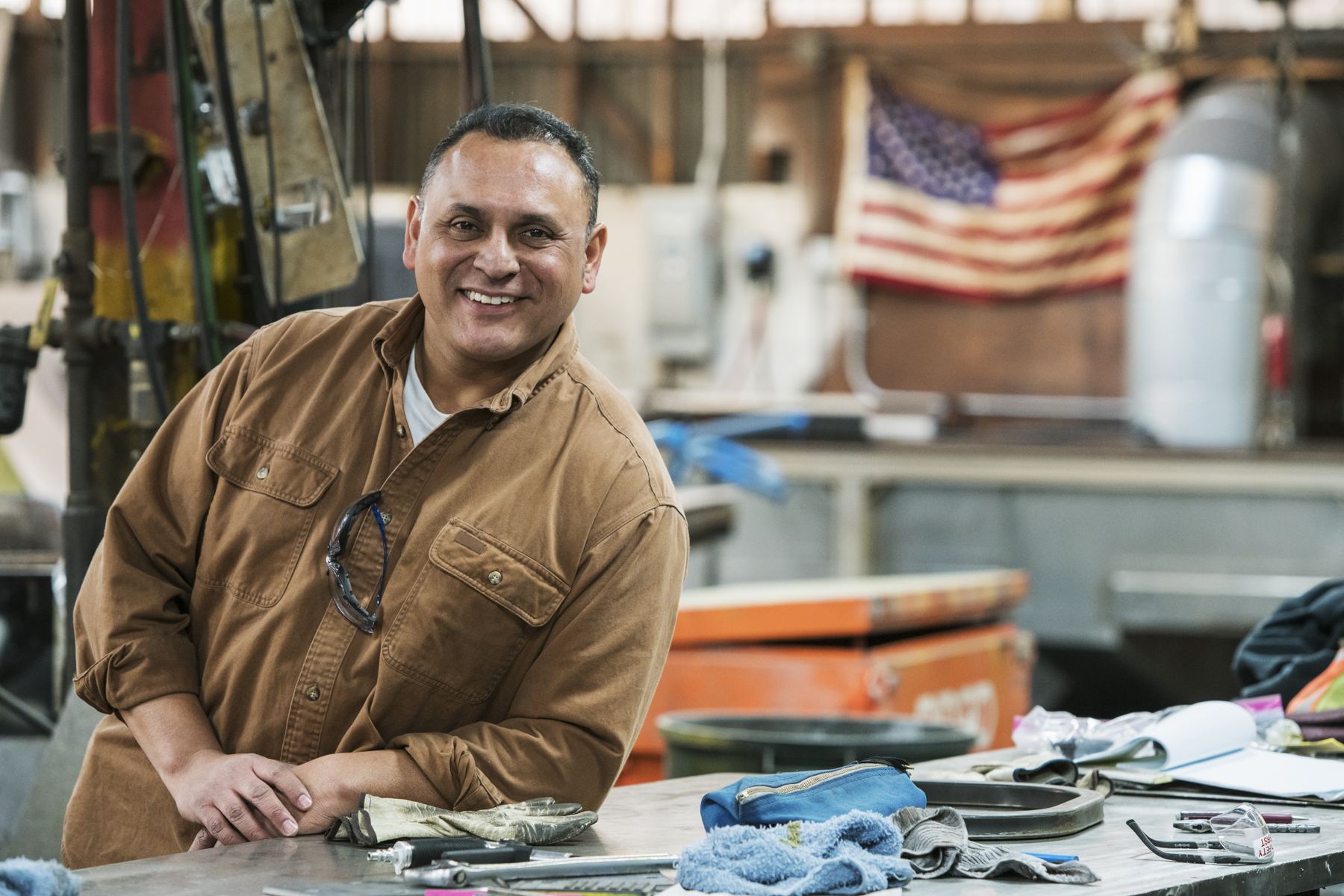 Small shop owner standing proudly in his workshop with an American flag